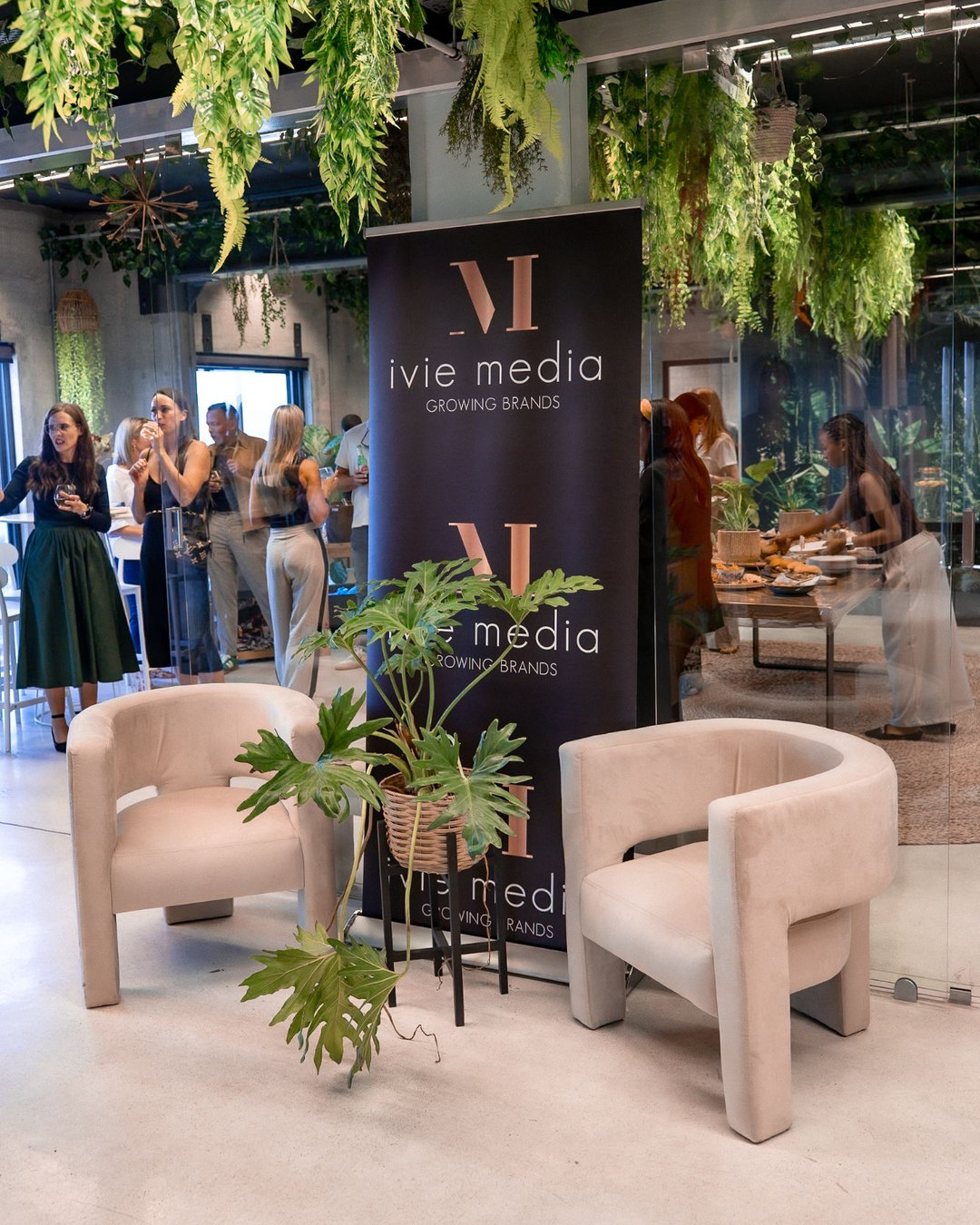 An Ivie Media event space with a branded banner, lounge chairs and hanging greenery
